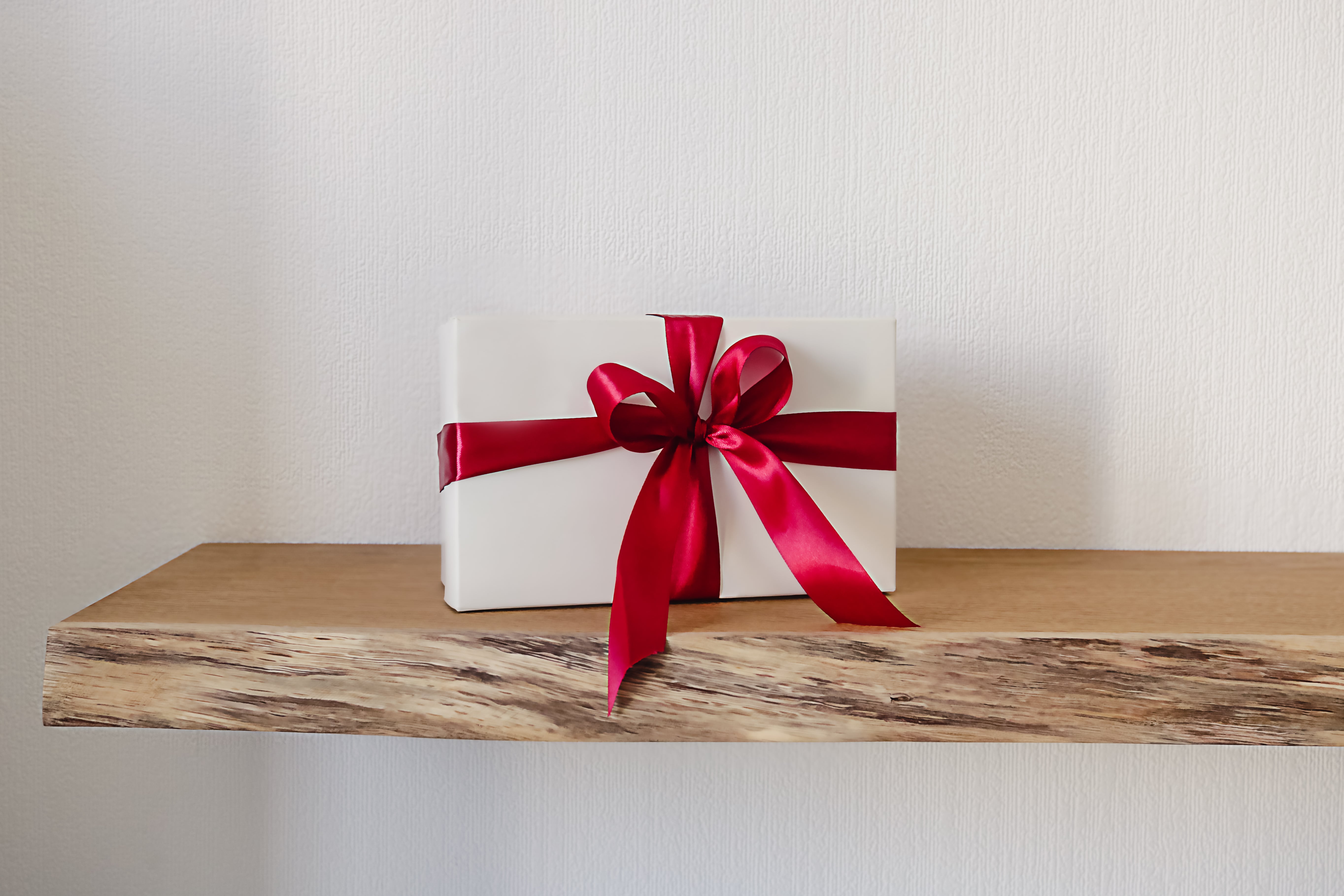 Small holiday gift box sitting on top of a wooden floating shelf