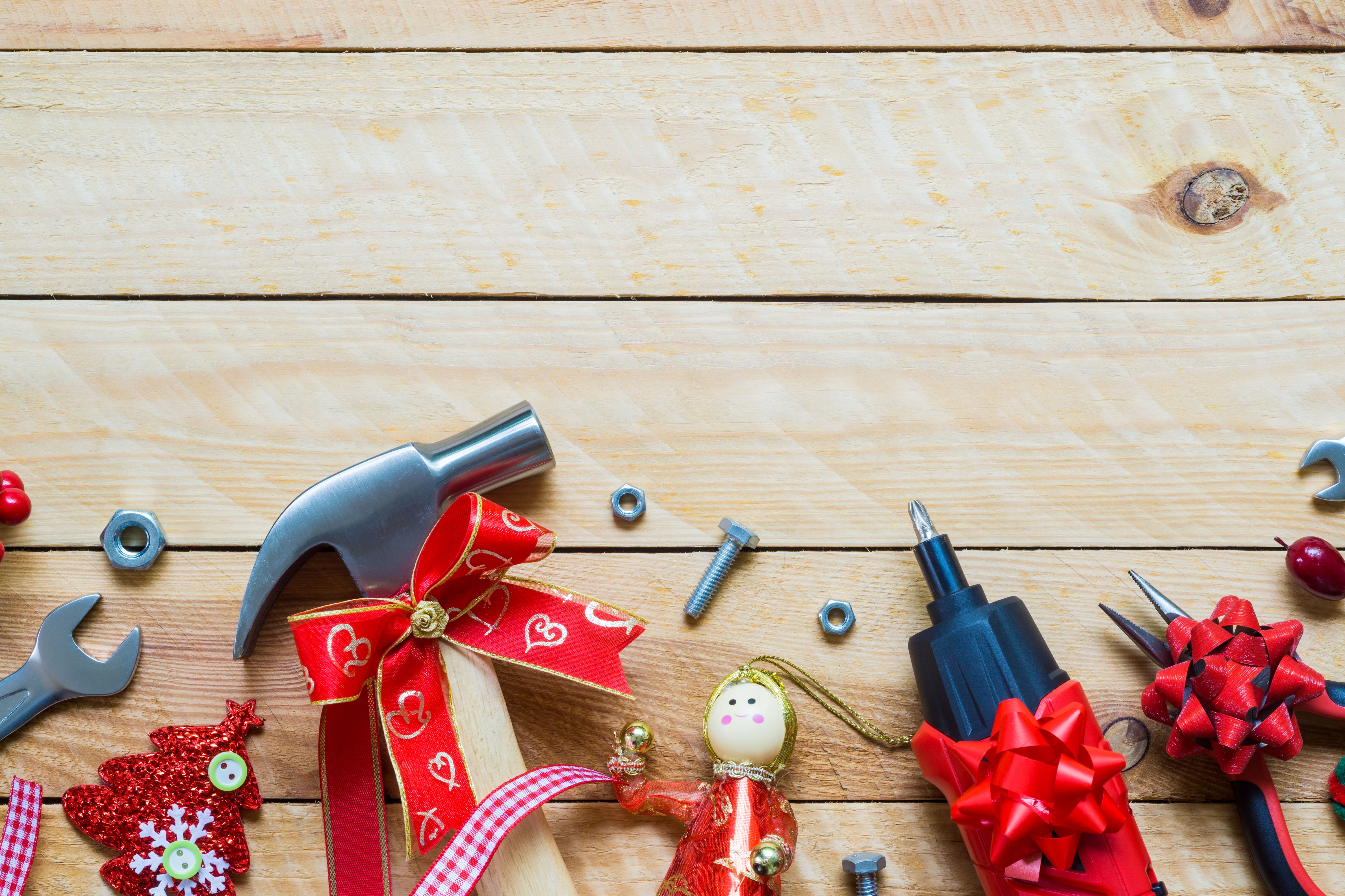 Flat lay of a wrench, a hammer, pliers, bolts, and screws with ribbon and bows in front of a wooden backdrop