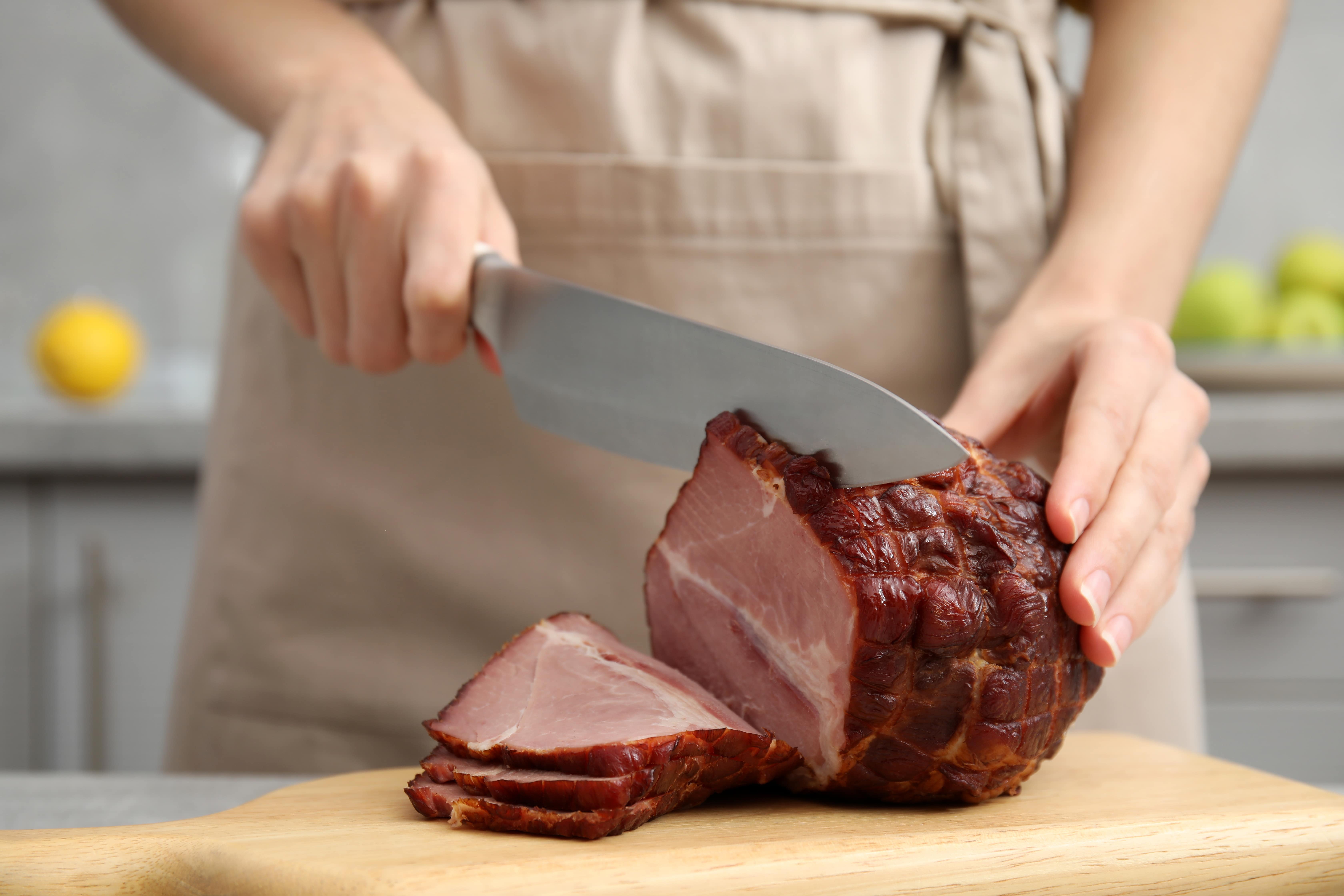 Close-up of someone carving a ham on top of a wooden cutting board